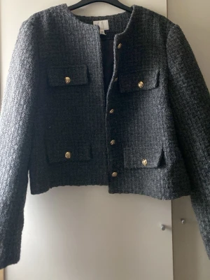 Mörkgrå kavajjacka från H&M - Passa mig som har storlek XS/S Säljer en mörkgrå kavajjacka från H&M i strukturerat tyg med fyra fickor framtill och guldknappar. Jackan har rak passform, rund halsringning och är helfodrad. Perfekt för dig som gillar klassisk men trendig stil.