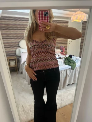 Zigzag-mönstrad linnetopp i rosa toner - Säljer en snygg linnetopp med breda axelband och ett färgstarkt zigzag-mönster i rosa, rött, beige och svart. Toppen har en söt detalj med liten rynkning vid bysten och är perfekt till sommaren. Materialet känns mjukt och följsamt.