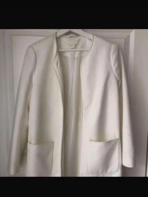 Vit kappa från H&M med fickor - Stilren vit kappa från H&M med raka linjer och två stora fickor framtill. Jackan är långärmad och har en öppen front utan knappar eller dragkedja. Perfekt för dig som gillar minimalistisk och clean stil.