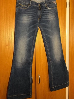  Replay flare jeans, storlek 30 blå denim - Säljer ett par blå Replay jeans med flare-ben och snygga slitningar. Klassisk femficksmodell med gul kontrastsöm och Replay-logga på fickan. Jeansen har en cool tvättad look och är tillverkade i slitstarkt denimtyg.