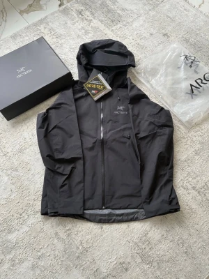 Helt ny Arc'teryx Beta LT (M, svart) - Säljer en helt ny Arc'teryx Beta LT i svart med huva och vattentätt Gore-Tex-material. Jackan har dragkedja framtill, logga på bröstet och justerbara detaljer vid huvan. Snygg, minimalistisk design och riktigt lätt och vattentätt material. Funkar för det mesta - hiking, skidåkning, vardag. Nypris 5 499. Etiketter och originallåda medföljer. (Storleken passade inte mig) 