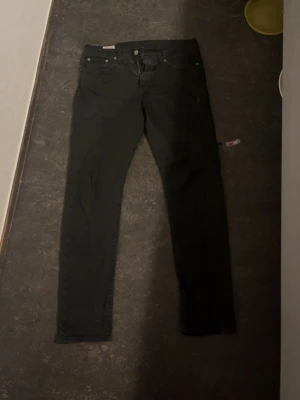 Svarta slimfit jeans från Levi's - Svarta jeans från Levi's med klassisk femficksdesign och skinny passform. Jeansen har en svart läderpatch bak i midjan och är tillverkade i stretchigt jeansmaterial för en tajt och bekväm känsla. Perfekta för dig som gillar en stilren look.