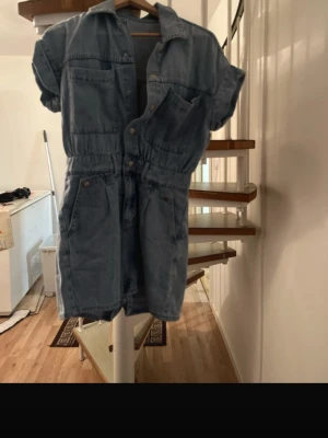 Denim Short Sleeve Playsuit / Romper - Blue denim playsuit with short sleeves and button-up front. Features chest pockets, elasticated waist for a flattering fit, and back pockets. Classic casual style – perfect for summer, everyday wear or festivals. • Size: XS • Color: Blue denim • Condition: Very good condition • Material: Denim • Fit: Fitted at waist, relaxed shorts • Closure: Buttons Smoke-free home. Feel free to message me if you want measurements 🌿 