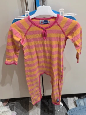 Randig rosa och gul väst från Molo - Säljer en färgglad väst från Molo i storlek 92. Västen har breda rosa och gula ränder, rund halsringning med en liten knappdetalj framtill och är tillverkad i mjukt bomullsmaterial. Perfekt för dig som gillar lekfull stil!