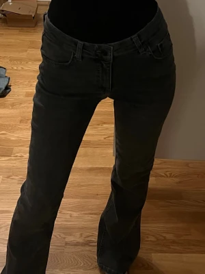 Grå bootcut jeans från Gina Tricot - Snygga grå jeans från Young Gina Tricot i bootcut-modell med klassisk femficksdesign och svarta detaljer. Jeansen har normal passform och är tillverkade i mjukt bomullsmaterial med lite stretch för extra komfort. Perfekt för dig som gillar en avslappnad men trendig look.