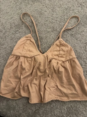 Beige linnetopp från Pull&Bear XS - Säljer en beige linnetopp från Pull&Bear i storlek XS. Toppen har tunna axelband, v-ringad skärning och volangdetaljer nedtill. Materialet är mjuk bomull och toppen är perfekt för varma dagar. Supersnygg att styla med jeans eller kjol!
