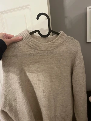 Beige stickad tröja från Gina Tricot - Mysig beige stickad tröja från Gina Tricot med rund halsringning och ribbade muddar vid ärmslut och nederkant. Perfekt för kyliga dagar och enkel att matcha med olika outfits.