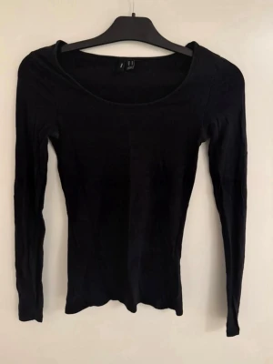 Svart långärmad topp Vero Moda - En enkel och stilren svart långärmad topp från Vero Moda. Modellen har rund halsringning och är figurnära i passformen. Tillverkad i mjuk bomull som känns skön mot huden. Perfekt att matcha med jeans eller kjol för en clean look.