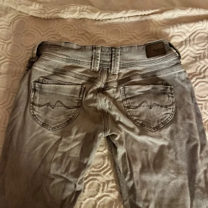 Pepe Jeans ljusgrå straight jeans - Snygga ljusgrå jeans från Pepe Jeans med klassisk femficksdesign och raka ben. Jeansen har diskreta sömmar, metallknappar och logotyp på bakfickan. Materialet är mjukt och stretchigt jeans, perfekt för en chill och stilren look.