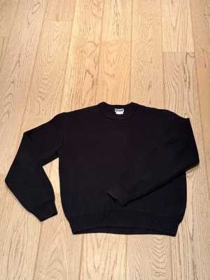 Svart stickad tröja från Weekday - Svart stickad tröja från Weekday i storlek S. Klassisk rund hals och ribbade muddar vid ärmslut och nederkant. Perfekt för lager-på-lager och enkel att matcha med jeans eller kjol. Stilren och tidlös design som funkar året runt.