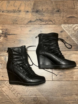 Svarta kilklackar med snörning - Snygga svarta boots med kilklack och snörning framtill. Skorna har dragkedja bak för enkel påtagning och är fodrade på insidan för extra värme.