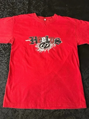 Röd Heelys t-shirt med tryck s( 140-146 cm längd)  - Säljer en röd t-shirt från Heelys med stort grafiskt tryck på bröstet i svart, vitt och rött. Klassisk rund hals och korta ärmar. Materialet känns som mjuk bomull, perfekt för dig som gillar streetwear och skate-vibe.