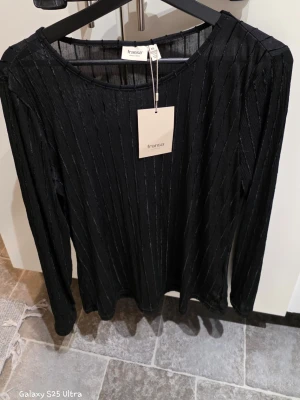 Svart randig långärmad topp Fransa XL - Säljer en svart långärmad topp från Fransa i storlek XL. Toppen har ett randigt mönster med tunna vertikala linjer och är tillverkad i mjuk polyester med lite stretch. Rund halsringning och lätt transparent känsla. Perfekt för dig som gillar stilrena detaljer.