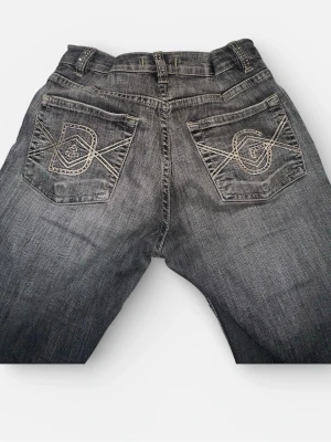 D&G svarta bootcut jeans med detaljer - Snygga svarta jeans från D&G med bootcut passform. Jeansen har coola broderade bakfickor med D&G-logga och nitar längs fickor och hällor. Materialet är klassisk jeans och färgen är tvättad svart med slitningar för en edgy look. 