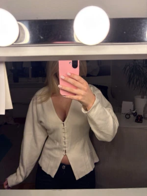 kofta från Gina Tricot - Säljer en beige v-ringad kofta från Gina Tricot i storlek M. Koftan har långa ärmar, knappar framtill och är lätt figursydd med en liten slits nedtill. 