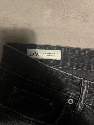 Svarta jeans från Zara, storlek 44 - Säljer ett par svarta jeans från Zara i storlek 44. Klassisk femficksmodell med raka ben och knappgylf. Jeansen har en mörk tvätt och är tillverkade i slitstarkt bomullsmaterial. Perfekt för dig som gillar enkel och stilren look.