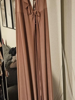 Gammelrosa  långklänning från ASOS - Säljer två gammelrosa  långklänningar från ASOS med omlott-design och snygg knytning framtill. Klänningen har volangdetaljer vid halsringningen och är tillverkad i ett mjukt, lätt material som ger ett elegant fall. Perfekt för dig som gillar stilrena och feminina plagg. Har en storlek 32 och en storlek 34. Prislapp kvar. Aldrig använda. 400 kr styck