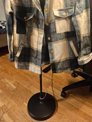 Rutig overshirt jacka från SHEIN - Säljer en rutig overshirt jacka från SHEIN i storlek XS. Jackan har stora beige och mörkgrå rutor, knappar framtill och på fickorna, samt två sidofickor. Materialet är mjukt och känns som ullblandning. Perfekt för lager-på-lager och chill stil.