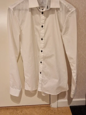 Vit skjorta från Bläck, tailored fit - Snygg vit skjorta från Bläck med tailored fit. Skjortan har svarta knappar 