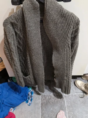 Grå stickad kofta från Zara - Säljer en grå, chunky stickad kofta från Zara i storlek L. Koftan har grova kabelstickade detaljer längs ärmarna och framstycket, samt bred krage och praktiska fickor. Perfekt för lager-på-lager och chill dagar.