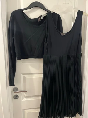 Svart plisserad klänning Phase Eight - Snygg svart klänning från Phase Eight i storlek 14. Klänningen har ärmlös överdel och ett plisserat kjolparti som ger en cool och modern look. Materialet känns mjukt och följsamt, perfekt för dig som gillar stilrena plagg med lite extra detalj. Passar med en croppad tröja över.