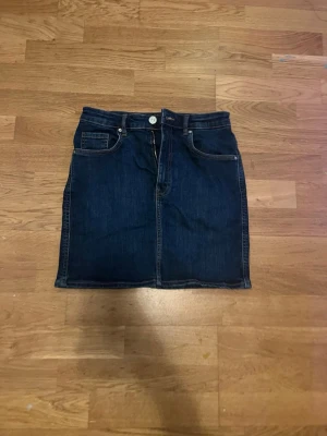 Mörkblå jeanskjol från Zara - Säljer en snygg mörkblå jeanskjol från Zara. Kjolen har dragkedja och en knapp där fram . I storlek s