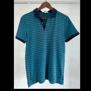 Randig blå-grön t-shirt från Calvin Klein - • Kortärmad blågrön Pikétröja från Calvin Klein i S. • 100% bomull. • Tvättad men oanvänd.