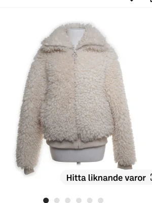 Beige teddyjacka med dragkedja - Säljer en fluffig beige teddyjacka med hög krage och dragkedja framtill. Jackan har långärmade ärmar och ribbade muddar vid nederkant och ärmslut. Perfekt för dig som vill ha en mysig och trendig look under kyliga dagar.