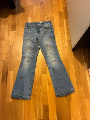 Blå bootcut jeans från JDY, W27 L30 - Snygga blå jeans från JDY med klassisk femficksdesign och bootcut-ben. Jeansen har normal passform och är tillverkade i mjukt denimtyg med lätt slitna detaljer. Perfekt för dig som gillar en avslappnad och trendig look.