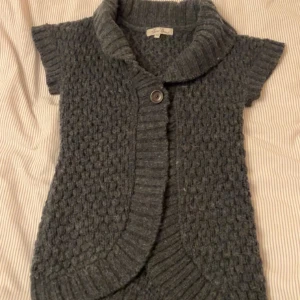 Grå stickad cardigan jacka Miss Snob - Säljer en grå stickad cardigan jacka från Miss Snob med korta ärmar och stor krage. Jackan har ett snyggt strukturerat mönster och stängs med en knapp framtill. Perfekt för lager-på-lager. Motsvarar en storlek xs!