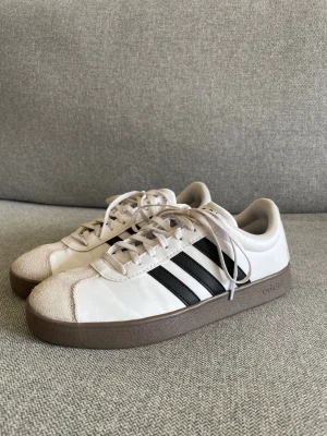 Adidas Samba sneakers vit/svart - Adidas Samba sneakers med vit ovandel i skinn, svarta ränder på sidorna och beige mockadetalj vid tån. Brun platt gummisula. 