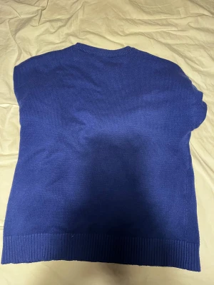 Blå stickad tröja Ami Paris med hjärta - Snygg blå stickad tröja från Ami Paris med vit hjärtdetalj och bokstaven A på bröstet. Tröjan har rund hals och ribbade muddar vid ärmslut och nederkant. Perfekt för dig som gillar stilrena och trendiga plagg med en twist.sitter perfekt på dig om du är ungefär 175cm