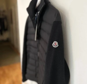 Äkta Svart Moncler cardigan  - Snygg svart pufferjacka från Moncler med quiltad front och stickade ärmar. Jackan har dragkedja framtill, två dragkedjefickor och klassisk Moncler-logga på ärmen. Perfekt för dig som vill ha en stilren och exklusiv look. ÄKTA!