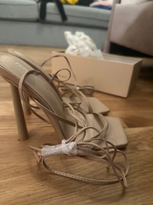 Beige sandaler med klack från Public Desire - Fyrkantig tå och tunna remmar som knyts runt foten. Passar inte mej, helt oanvända och kartong medföljer!