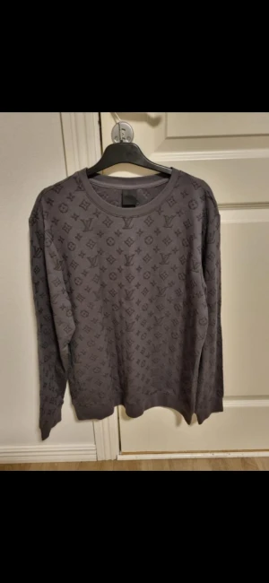 Grå Louis Vuitton långärmad tröja - Snygg grå långärmad tröja från Louis Vuitton med det klassiska LV-monogrammet över hela plagget. Rund halsringning och mjukt material som känns skönt mot huden. Perfekt för dig som gillar exklusiva streetwear-vibbar och vill sticka ut med designerplagg.