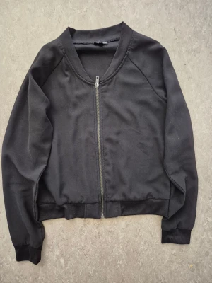 Jacka/Kofta - Svart jacka/Kofta från KappAhl i storlek 158/164. Jackan har en klassisk rak passform, ribbade muddar och dragkedja framtill. Materialet är mjukt och känns som bomull, perfekt för en chill look. Enkel och stilren design utan mönster eller extra detaljer. Har en fläck bara.