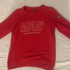 Röd och blå sweatshirt från Replay - Snygg röd och blå sweatshirt från Replay med stort tryck på bröstet och en cool logotyp på ärmen. Tröjan har rund hals, långa ärmar och ribbade muddar. Perfekt för dig som gillar streetwear och vill sticka ut med en bold färg. 