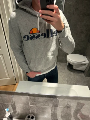 Grå Ellesse hoodie med logga - Säljer en grå hoodie från Ellesse. Riktigt bra skicka då den knappt använts. Jag på bilden är 188cn och bör storlek S. Hör av er vid frågor :)