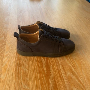 Mörkblå sneakers med röd sula - Säljer ett par mörkblå sneakers från Christian Louboutin i mocka med klassisk röd sula. Skorna har rund tå, snörning och diskreta sömdetaljer. Insidan är fodrad i ljust skinn och yttersulan har den ikoniska Louboutin-signaturen. Storlek 41 passar 42. Påse ingår