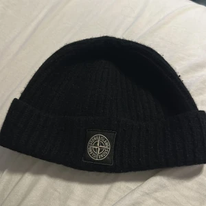 Svart mössa från Stone Island - Svart Stone island mössa köpt på NK i Göteborg för ungefär 5-6 år sedan. Den har dock råkat slängas in i tvätten och krympt en del, därför hade den nog passat bättre på dig som har ett lite mindre huvud, elelr om du vill att den ska sitta nästan lite som en skull cap.