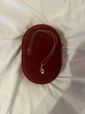 Guldfärgat halsband med pärlhänge - Snyggt guldfärgat halsband med tunn kedja och ett hänge i form av en vit pärla omsluten av guldfärgade detaljer. Kedjan är enkel och klassisk, och hänget ger en elegant touch. Perfekt accessoar för att lyfta din outfit.