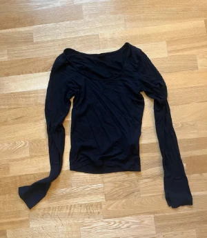 Svart långärmad topp Gina Tricot - En svart långärmad topp från Gina Tricot i storlek S. Toppen har en djupare rundad halsringning och är figurnära i modellen. Tillverkad i mjukt och stretchigt material som känns skönt mot huden. Perfekt att styla med jeans eller kjol.