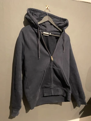 Mörkblå Carhartt hoodie med dragkedja - Snygg mörkblå hoodie från Carhartt med dragkedja, stor huva och snören. Mjuk insida och klassisk känguruficka framtill. Carhartt-logga i gult på vänster ärm. Perfekt för chill dagar och streetwear-stil. In princip oanvänd. Kontakta mig om ni har några frågor! MVH Gustav🙂