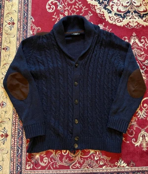 Mörkblå stickad kofta med mockadetaljer - Säljer min ascoola kabelstickade marinblåa kofta med mockadetaljer. Perfekt nu under vintern ❄️  Den har en liten defekt som knappt syns vid knappen längst ner(se bild 3), samt är lite nopprig men det går lätt att fixa 👍Storlek M. Hör av er vid funderingar 🙌