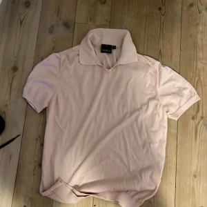 Ljusrosa pikétröja Oscar Jacobson - Snygg ljusrosa pikétröja från Oscar Jacobson, tillverkad i Italien. Tröjan har klassisk krage och korta ärmar, perfekt för dig som gillar stilrena och softa färger. Materialet känns mjukt och lyxigt mot huden.