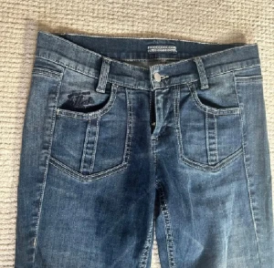 Blå bootcut jeans med låg midja - Säljer ett par blå jeans med bootcut och låg midja. Jeansen har markerade sömmar, klassiska fickor fram och bak samt en snygg tvättad look. Innerbenslängd 82 cm, midjemått 38 cm