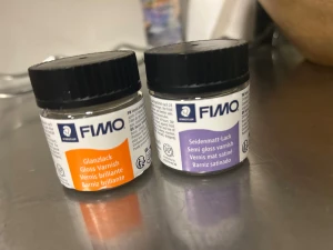 FIMO Glanslack & Seidenmatt-Lack - Två burkar lack från FIMO, en med orange etikett för glansig finish och en med lila etikett för semimatt resultat. Båda har svart skruvlock och är perfekta för att ge yta och glans till kreativa projekt. Materialet är flytande lack i små plastburkar. Den glansiga är ca 80% kvar i och den matta har 90% kvar i. 