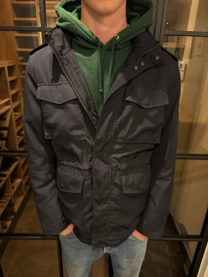 Mörkblå parkajacka med fickor - Parkajacka från j.lindeberg i mörkblå färg med fyra stora fickor framtill, axelklaffar och dragkedja. Skön inför vintern! Skick: acceptabelt pris: 1199kr 