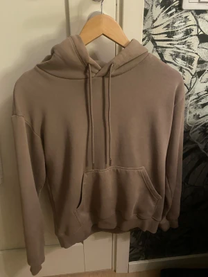 Beige oversized hoodie med ficka - Säljer en beige hoodie med huva och dragsnören. Hoodien har en stor magficka och ribbade muddar vid ärmslut och nederkant. Den har en liten fläck som man knappt ser! 