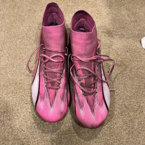 Puma Ultra rosa fotbollsskor strl 45 - Säljer ett par Puma Ultra fotbollsskor i storlek 45. Skorna har en snygg rosa färg med svarta och vita detaljer samt ett randigt mönster. De har snörning och en smal, strömlinjeformad siluett som passar perfekt för snabba spelare. Materialet är lätt syntet för bästa känsla på planen.